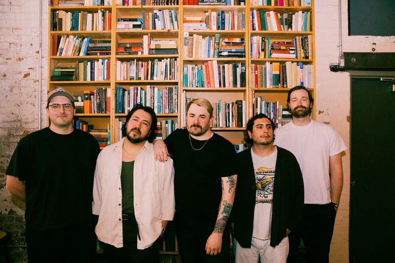 Rock band Free Throw standing in front of large bookshelves packed with books, photographed by Imani Givertz.